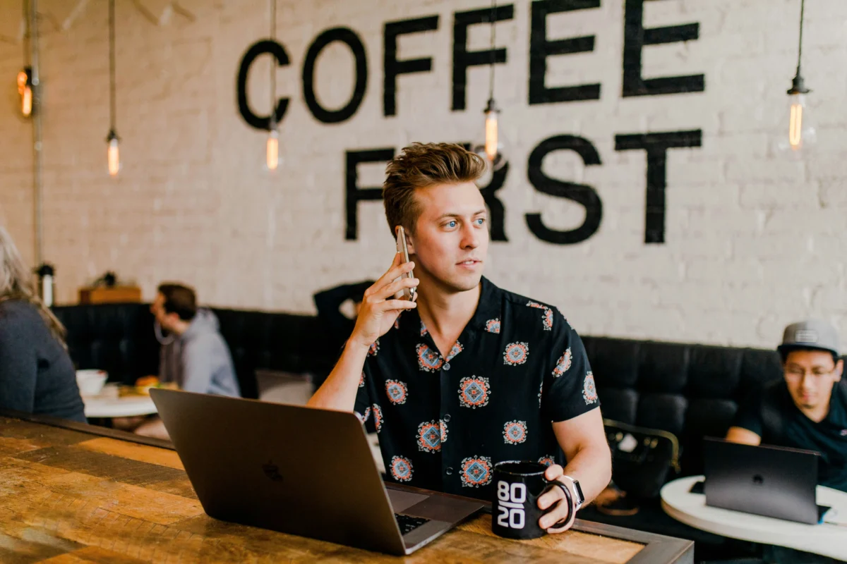 A man wearing a stylish white button-down shirt, paired with tailored navy trousers, sitting in a modern office setting.