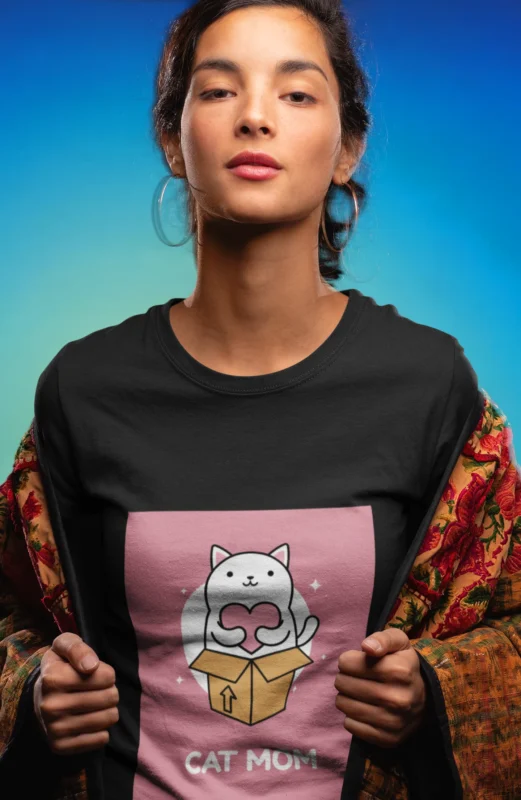 Woman wearing a "Cat Mom" t-shirt, smiling and cuddling her cat.