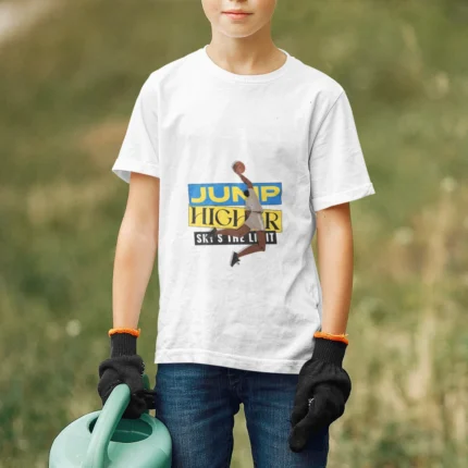 A young boy wearing the NBA "Jump Higher, Sky Is the Limit" t-shirt, leaping with a basketball under a vibrant sky, symbolizing determination and ambition.