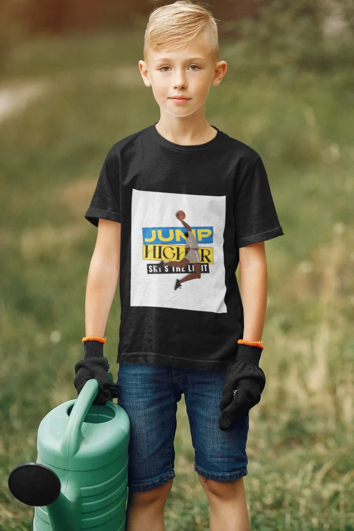 A young boy wearing the NBA "Jump Higher, Sky Is the Limit" t-shirt, leaping with a basketball under a vibrant sky, symbolizing determination and ambition.